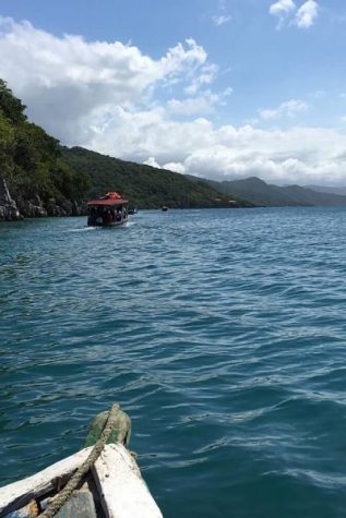 A boat (bottom left) follows another tourist boat as they pass looming mountains on their way to a secluded beach in Haiti.