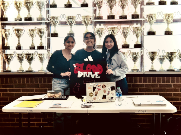 This image shows Samhitha Kamchanapelly (left), Arpita Jagga (center), and Dia Patil (right) posing for a photo behind the HOSA blood drive stand. HOSA got recognized last year for chapter of the year and hope to get a bigger award this year. Eera Ingle/The Lambert Post